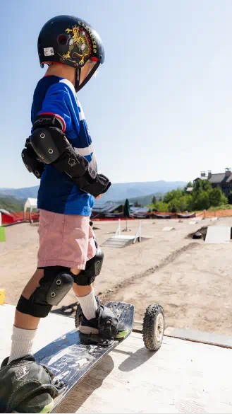 little boy stands on a skateboard on a ramp at Camp Aspen Snowmass 