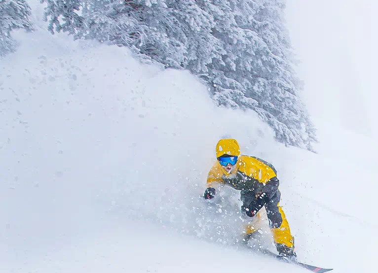 Snowboarder through powder on Aspen mountain, snow billows up behind him 